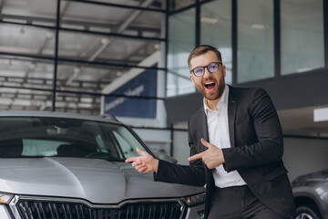 Yes, that's my new car! Customer in car dealership. Happy bearded man new car owner raises his...