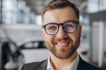 Close-up portrait of bearded businessman in glasses smiling and suit at car dealership