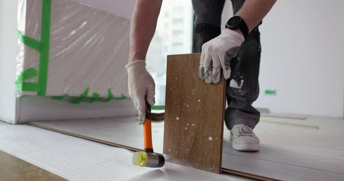 Carpenter lays laminate and taps with hammer for quality installation. Floor covering repair