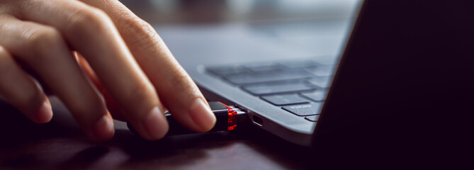 Hand holding usb flash drive with connecting to laptop at wooden table