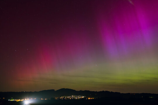 Mesmerizing Northern Lights with Purple, Violett and Green Hues over a buisy Village lights and hilly region