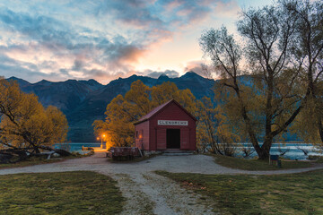 Wooden red building of boat shed Glenorchy in autumn forest by Lake Wakatipu in the evening