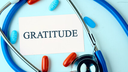Concept GRATITUDE written on a white business card on a blue background with a stethoscope, pills...