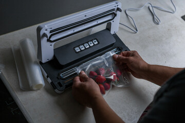 a man's hand is using a vacuum machine to vacuum pack strawberries into plastic bags. 