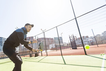 Man playing padel in a green grass padel court indoor behind the net