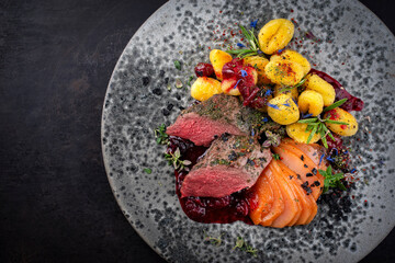 Traditional fried venison back filet with saturated pear, gnocchi and plum jam served as top view on Nordic design plate with copy space