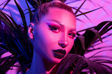 Fashion model woman with a bright make-up in colourful bright neon uv lights posing in studio.