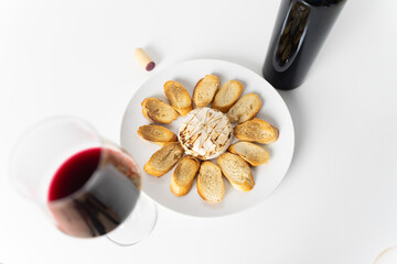 A glass of wine with Brie cheese baked in the oven and bread toasted on a plate on a white...