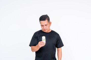 A middle aged Asian man wearing a black shirt stands against a white background, intently reading a Vitamin E bottle.