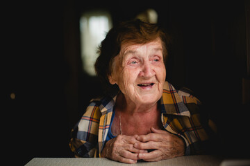 An elderly woman, her face reflecting a myriad of emotions, sits at the table.