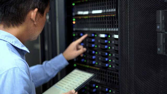 A technician in a blue shirt uses a tablet while inspecting a server rack in a modern data center, ensuring proper functionality.