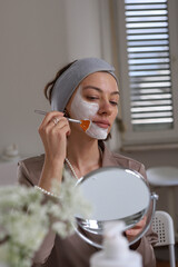 Woman in her room making facial mask holding mirror.Morning skin care routine. 