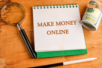 Business concept. MAKE MONEY ONLINE lettering written on a notebook with a magnifying glass and a...