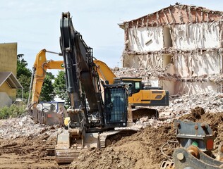 Two heavy excavators with a building under demolition on behind. Front view.