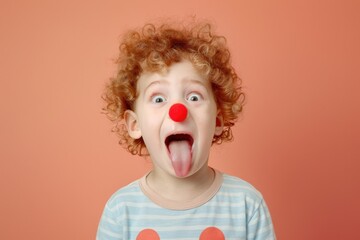 Humorous kid with red nose makes funny face against peach background.