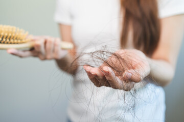 Hair fall problem concept. Shocked Asian woman looking at many hair lost in her hand and comb.