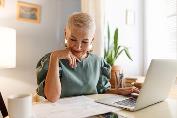 Senior female general accountant working with paper documents sitting at table in her office or...