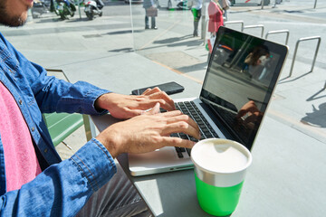 unrecognizable hands of a man sitting in a coffee shop using his laptop for work or chatting