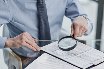 Businessman looking through a magnifying glass to documents