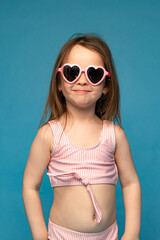 Happy child girl in pink swimsuit on a colored blue background. Travel, summer beach concept.