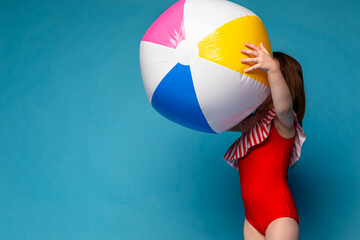Unrecognizable little girl wearing red swimsuit holding beachball on blue background. Summer...