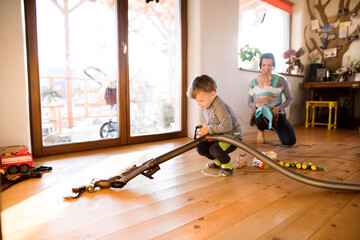 Young son helping mother with hosehold chores, vacuuming and cleaning their house. Weekly chores,...