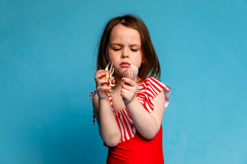 Little girl holding seashell in her hands on blue background. Girl on studio background. Child put...