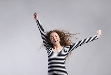 Portrait of a gorgeous teenage girl with curly hair, hands up. Studio shot, white background with...