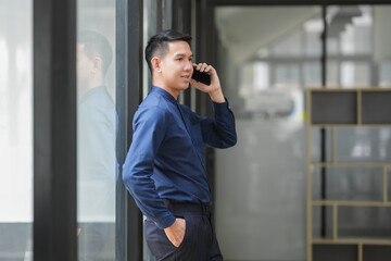Businessman in blue shirt talking on phone outside office building, representing communication and...