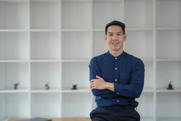 Confident young professional businessman standing with arms crossed in a modern office with white...