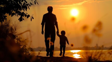Fototapeta premium Silhouette of father holding his child's hand walking into the sunset. Fatherhood, parenting concept