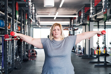 Overweight woman exercising in gym, using dumbbells.