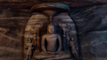 A close-up view of a historic Buddha statue carved inside a rock cave.