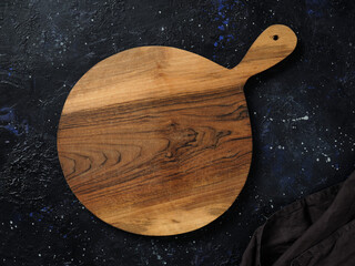 Top view of empty round wooden cutting board with handle on abstract dark background.