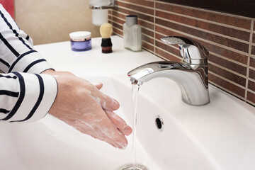 Close-up of a man in a business shirt washing his hands in his home bathroom after work.