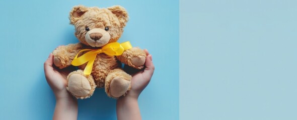 Photo of a person holding a teddy bear with a yellow ribbon around its lowered head, on a light blue background. Web banner with a wide angle view.