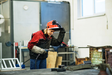 Beautiful blonde woman works as a welder in workshop, operating welding machine, wearing protective...