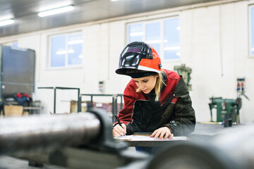 Beautiful blonde woman works as a welder in workshop, operating welding machine, wearing protective...