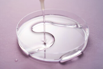Serum or cosmetic oil flows into a transparent bowl on a purple background.