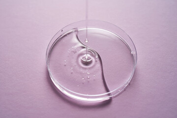 Serum or cosmetic oil flows into a transparent bowl on a purple background.