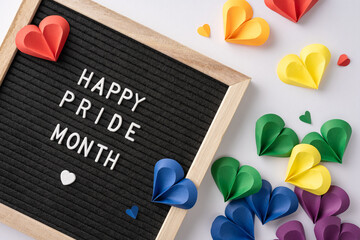 Black board with Happy Pride Month message surrounded by colorful paper hearts celebrating LGBTQ+ rights and diversity