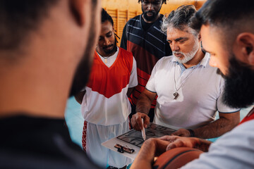 Mature coach and a diverse basketball team in huddle discussing game tactic