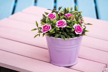 Artificial colorful flowers in decorative flowerpots on blue , pink wooden background