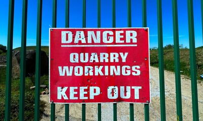 A faded red and white sign warning, of danger from quarry workings is attached to a green metal...