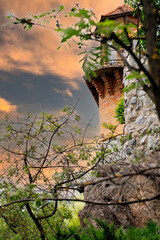 monumental red stone tower, branches of trees on the background of the sunset, stone fortification