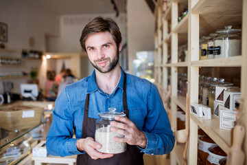 Handsome man working in package-free store using reusable containers. Zero waste shops offering...