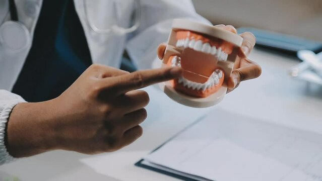 Online medical consultation. Asian male dentist doctor showing jaw model educate about taking care of gums and teeth through talking online, making video call with patient. Medical and technology