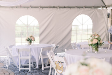 A tented wedding reception with white tables and flowers on each table. 