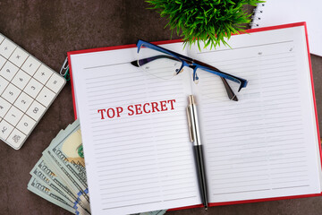 The sentence, Top Secret, written on the open page of the business notebook next to eyeglasses, a...