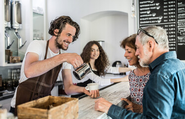 Handsome barista working in coffee shop, serving customers, elderly couple. University student working part-time in cafe.